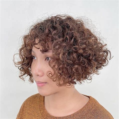 Curly short hair with fringe - An asymmetrical pixie for women over 50 is perfect for fine hair textures. This layered cut with longer hair on the one side creates a younger-looking version of you. The nape of your hair should be cut short to highlight the edgy asymmetry of the cut. It’s best styled flat and will make the most out of your limp locks.
